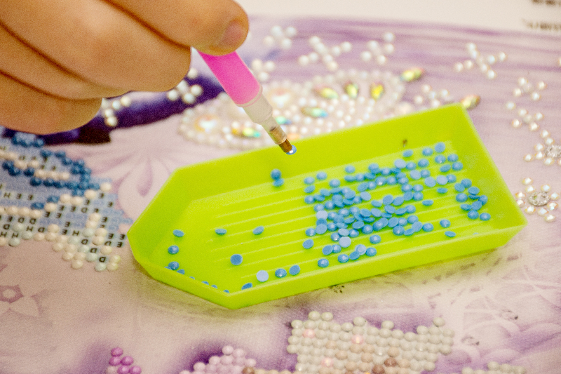 Person placing resin drills onto a diamond painting canvas